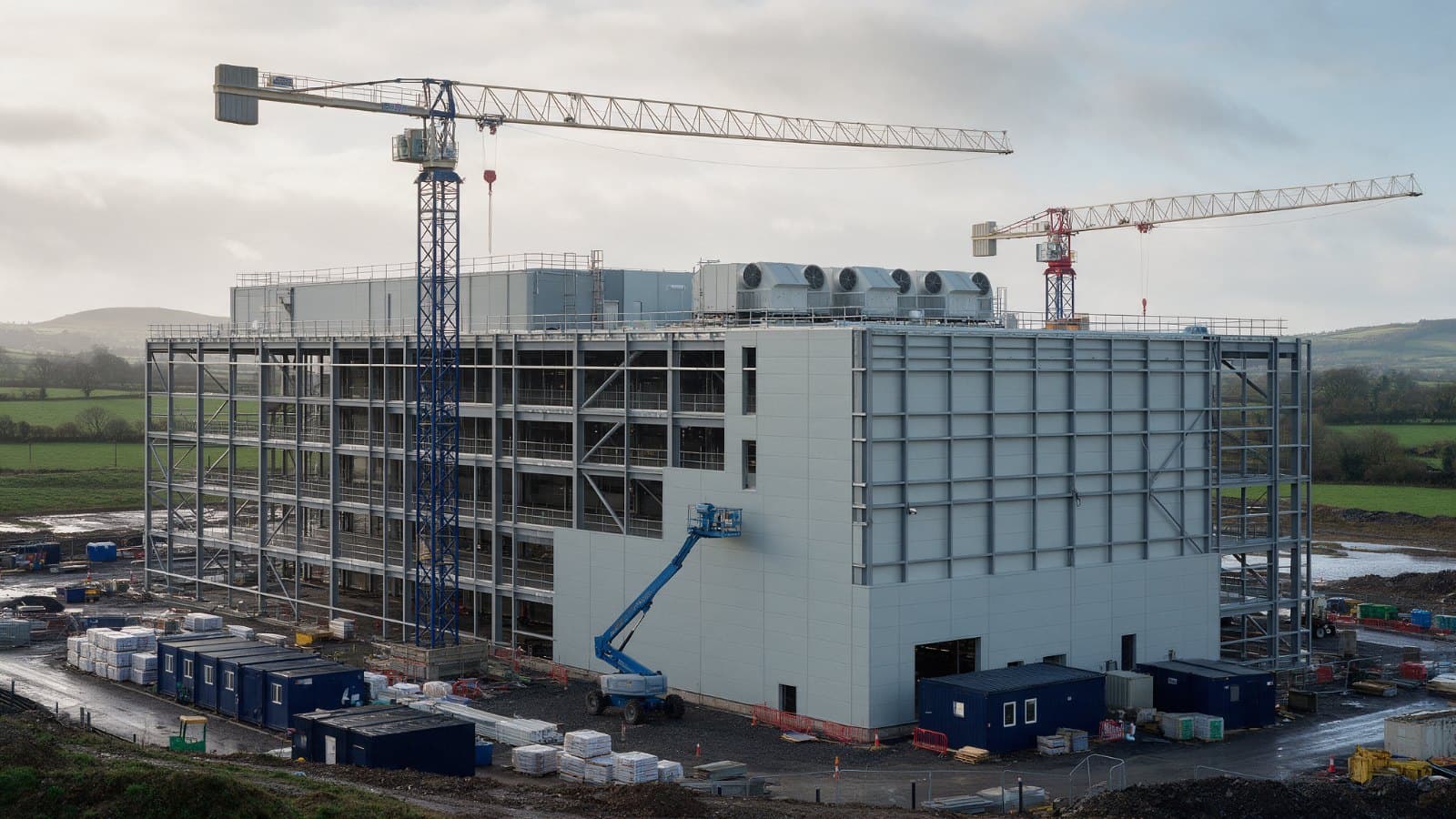 New pharmaceutical manufacturing building under construction in green countryside with two tower cranes